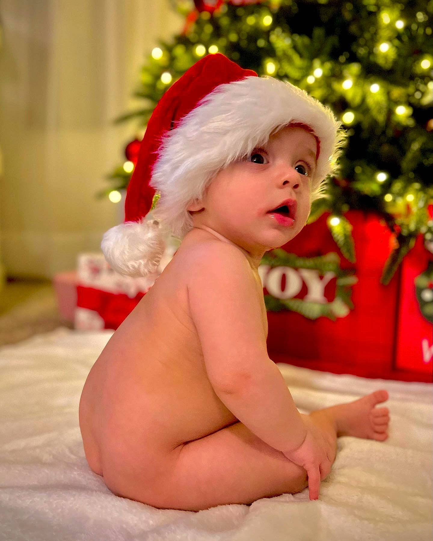 Landen is registered to the contest to win money with this photo: baby, child, christmas_ornament, christmas_tree, event, face, facial_expression, foot, fun, happy, hat, head, headwear, holiday, human_body, lap, person, santa_claus, smile, standing
