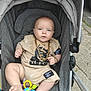 baby, stroller, child, gold_chain, toy, beige_clothing, outdoor, footwear, expression, person, infant, sitting, accessory, cute, casual, street, play, hand, foot, portrait
