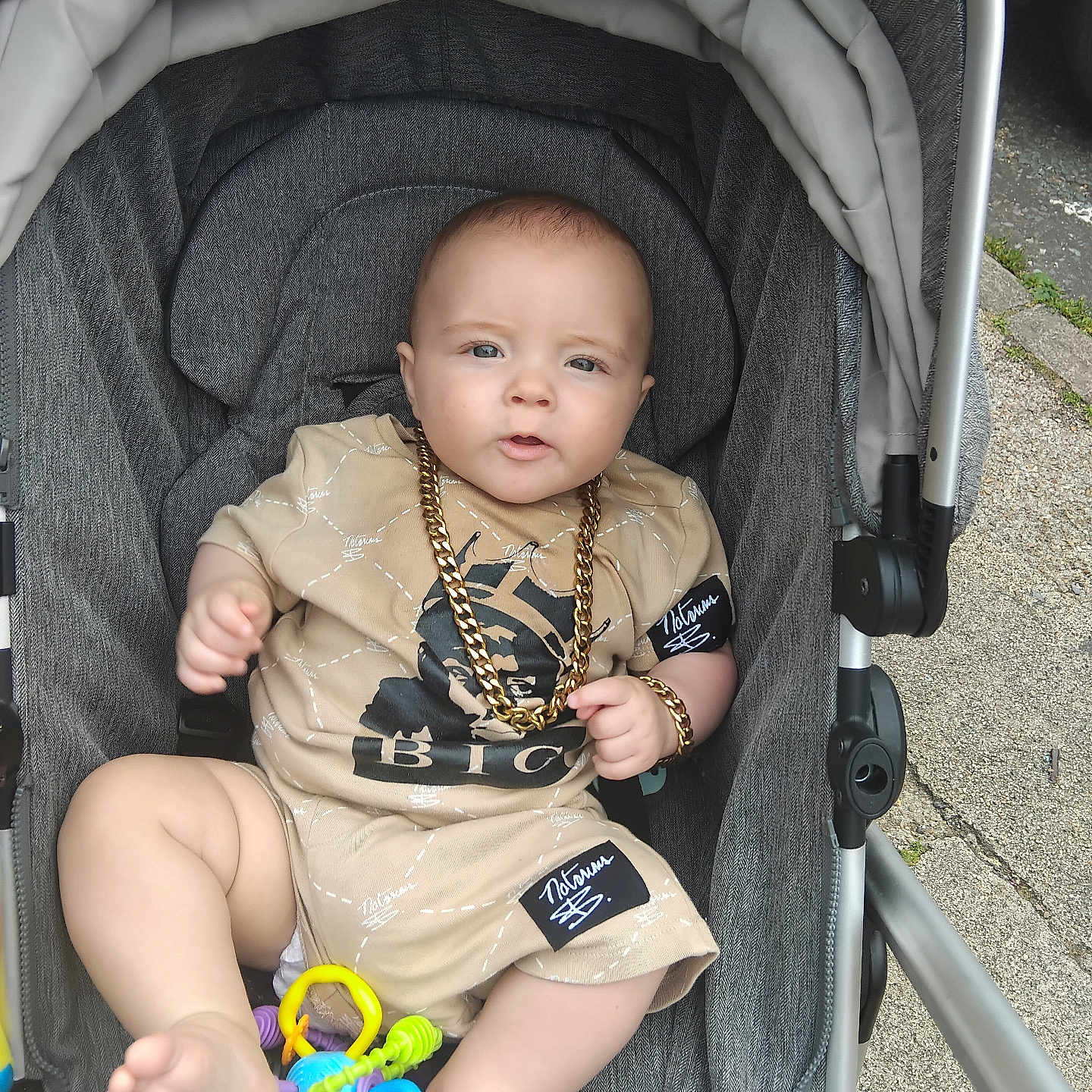 Grayson-Jo joined the competition — help win amazing prizes! accessory, baby, beige_clothing, casual, child, cute, expression, foot, footwear, gold_chain, hand, infant, outdoor, person, play, portrait, sitting, street, stroller, toy