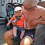 Grayson-Jo joined the competition — help win amazing prizes! baby, man, child, outdoor, sunlight, stroller, cap, orange_shirt, glasses, shorts, bare_chest, chair, concrete, door, window, hand, footwear, family, summer, portrait