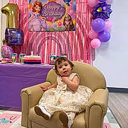 Sofia joined the competition — help win amazing prizes! toddler, birthday_party, balloons, cake, birthday_candle, armchair, dress, child, indoor, celebration, banner, princess_theme, purple_tablecloth, floor_mat, party_decorations, smiling, young_child, festive, happy, seated