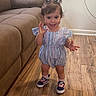 toddler, child, indoor, standing, smiling, romper, sneakers, wooden_floor, couch, brown_couch, hair_pigtails, happy, person, flooring, home, baby, cute, young_child, casual_clothing, portrait