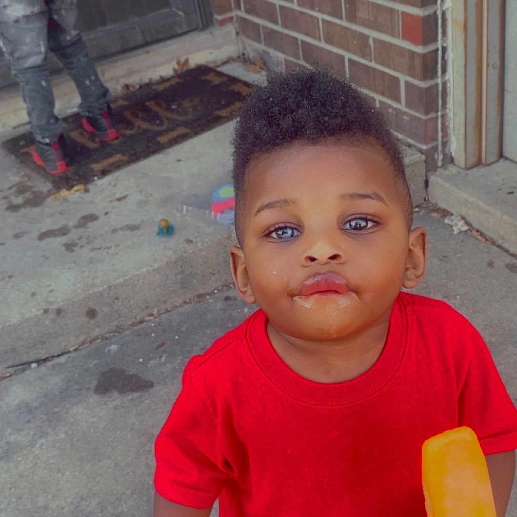 Artist joined the competition — help win amazing prizes! background, black_pants, brick_wall, child, concrete, curly_hair, door, expression, face, footwear, ice_pop, outdoor, person, play, red_shirt, sidewalk, snack, standing, summer, toddler