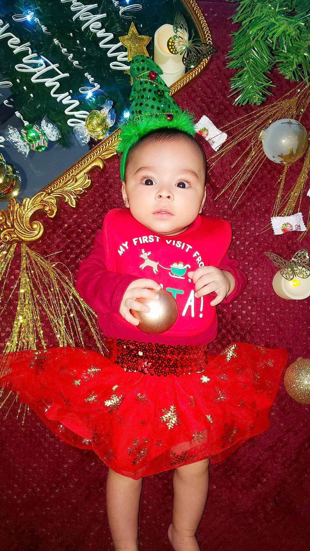 Nehemiah is registered to the contest to win money with this photo: baby_toddler_clothing, cheek, christmas, christmas_decoration, christmas_ornament, christmas_tree, event, green, happy, head, holiday, holiday_ornament, human_body, magenta, ornament, people_in_nature, person, pink, red, toddler