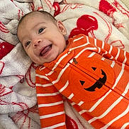 Jocelyn is registered to the contest to win money with this photo: baby, infant, smiling, orange_clothing, striped_clothing, jack_o_lantern, blanket, soft_texture, red_and_white, happy, lying_down, cute, portrait, child, young, cozy, indoors, warm, face, expressive