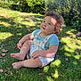 baby_clothes, barefoot, blue_shirt, child, curly_hair, cute, daylight, garden, grass, greenery, happy, innocence, nature, outdoor, portrait, shorts, sitting, summer, sunlight, toddler