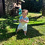 baby, barefoot, blue_sky, child, clapping, clothing, curly_hair, daylight, garden, grass, greenery, nature, outdoor, person, playful, shadow, summer, sunlight, tree, wooden_shed