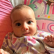 Naomi is registered to the contest to win money with this photo: baby, infant, face, eyes, onesie, hand, patterned_clothing, rainbow, monkey, pink, purple, green, background, cute, child, portrait, indoors, colorful, expression, curious