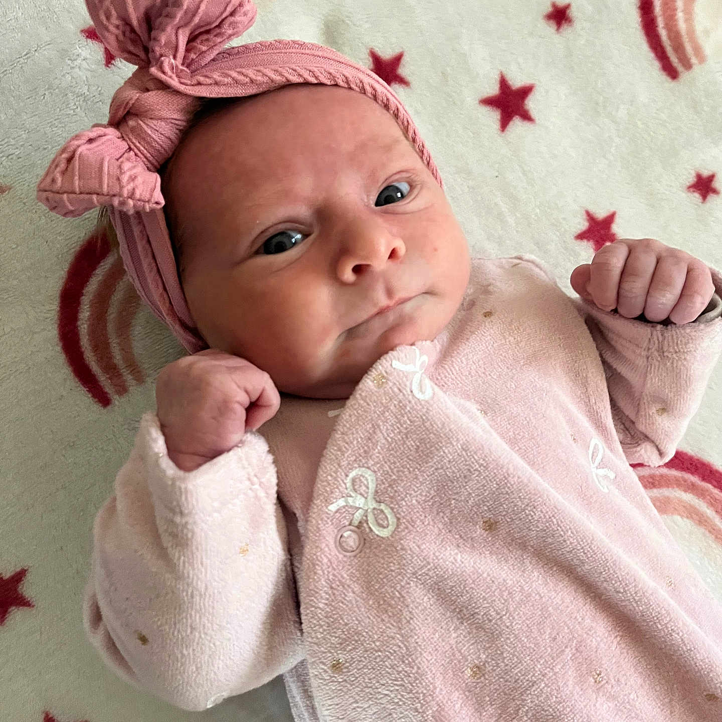 Maude a rejoint le concours — aidez-le/la à gagner de superbes lots ! baby, infant, pink_bow, headband, pink_outfit, blanket, stars, rainbows, face, fist, newborn, lying_down, cute, child, portrait, soft_texture, cozy, expression, indoors, sleepwear