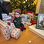 baby, child, christmas_tree, christmas_lights, presents, gift_wrap, holiday, elf_costume, red_socks, striped_hat, living_room, floor, hand, framed_photo, couch, decorations, festive, indoors, person, celebration