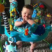 Jace is registered to the contest to win money with this photo: baby, child, activity_jumper, toy, colorful, indoor, carpet, smiling, happy, playtime, cute, infant, legs, hands, face, blue_clothing, plush_toy, background, furniture, homedecor