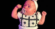 Brynnlee is registered to the contest to win money with this photo: baby, infant, child, portrait, pacifier, headband, dress, ruffles, fists, arms_up, serious_expression, looking_sideways, face, skin, fashion, studio, black_background, close_up, costume, photography
