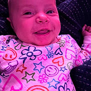 Brynnlee is registered to the contest to win money with this photo: baby, infant, child, smiling, portrait, close_up, face, head, eyes, nose, mouth, floral_pattern, colorful_clothing, pink, purple_lighting, sitting, indoors, blanket, happy, photograph
