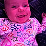 baby, infant, child, smiling, portrait, close_up, face, head, eyes, nose, mouth, floral_pattern, colorful_clothing, pink, purple_lighting, sitting, indoors, blanket, happy, photograph