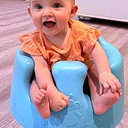 Isabelle is registered to the contest to win money with this photo: baby, infant, smiling, blue_baby_seat, orange_clothing, happy, indoors, flooring, child, cute, sitting, small_toddler, toes, face, person, home, floor, bright, expression, seat