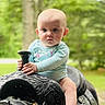 Isabelle is registered to the contest to win money with this photo: baby, child, outdoor, saddle, horse_tack, greenery, nature, portrait, infant, hand, face, head, barefoot, sitting, blue_clothing, expression, young_child, daylight, person, grip