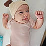 Annelisse joined the competition — help win amazing prizes! baby, infant, cute, hat, clothing, smile, tongue, raised_hands, lying_down, onesie, red_bracelet, face, cheeks, skin, expression, child, indoors, soft, adorable, playful