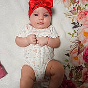 Annelisse joined the competition — help win amazing prizes! baby, infant, headband, red_bow, onesie, heart_pattern, blanket, floral_pattern, lying_down, fist, cute, child, soft_texture, indoors, portrait, skin, person, newborn, expression, adorable