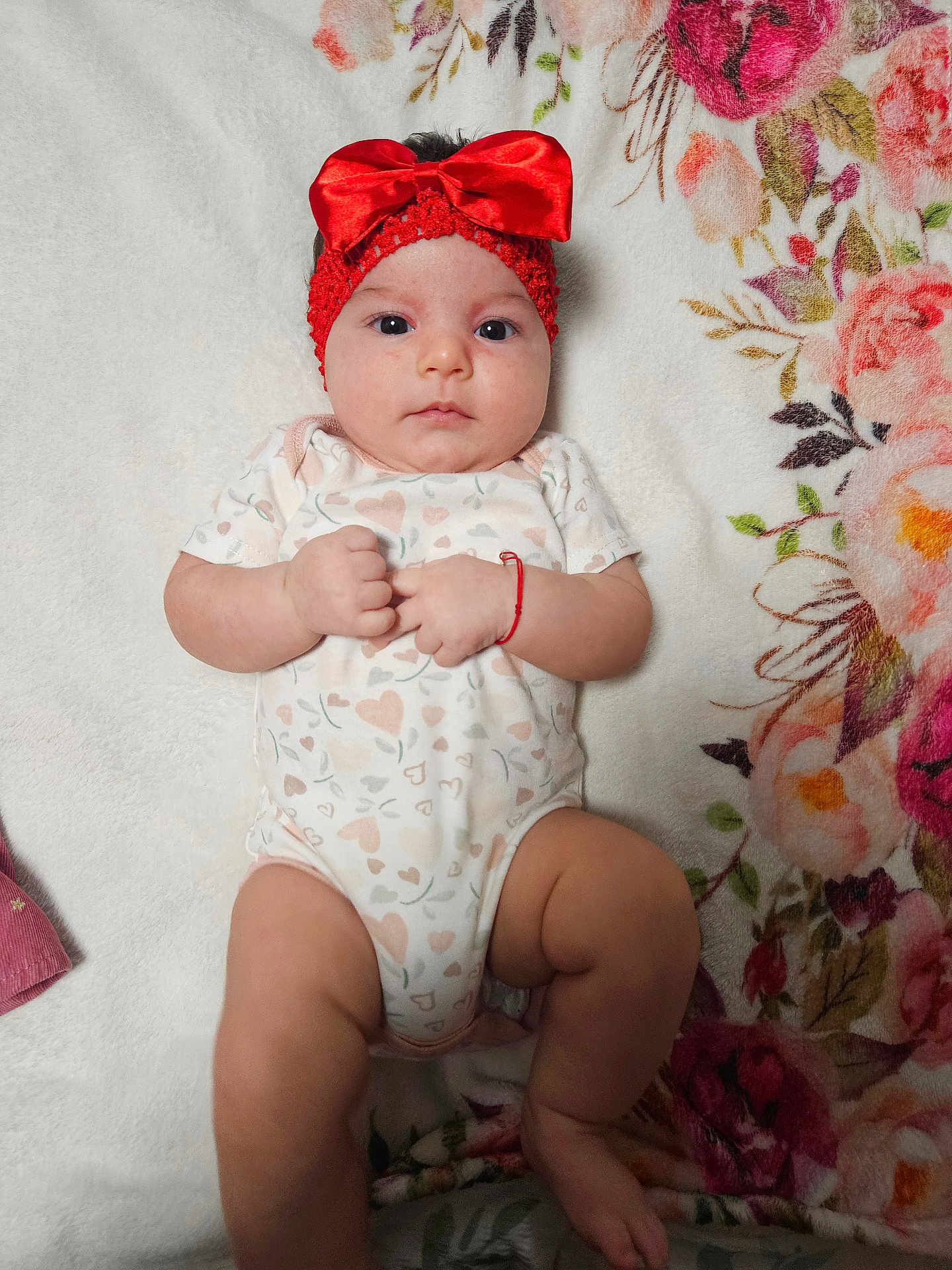 Annelisse joined the competition — help win amazing prizes! baby, infant, headband, red_bow, onesie, heart_pattern, blanket, floral_pattern, lying_down, fist, cute, child, soft_texture, indoors, portrait, skin, person, newborn, expression, adorable
