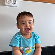 Yahya participe au concours pour gagner de l'argent avec cette photo : baby, child, happy, smiling, blue_shirt, cupcake_print, sitting, cross_legged, indoor, countertop, black_surface, white_wall, wooden_panel, holding_object, cute, portrait, infant, toddler, person, playful