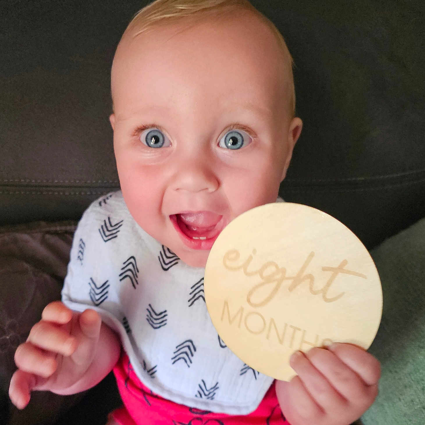 Pj is registered to the contest to win money with this photo: baby, bib, blue_eyes, child, closeup, couch, cute, eight_months, face, hand, happy, holding, indoor, infant, person, portrait, shorts, sitting, smiling, wooden_sign