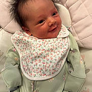 Heidi joined the competition — help win amazing prizes! baby, smiling, face, hair, onesie, bib, floral_pattern, green_clothing, lying_down, quilted_surface, infant, cute, happy, portrait, child, newborn, soft_lighting, indoors, cozy, toddler