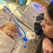 Rayleigh is registered to the contest to win money with this photo: baby, infant, hospital, medical_equipment, tubes, patient, caregiver, woman, bed, blanket, healthcare, monitoring, love, concern, medical_treatment, intensive_care, face, person, resting, newborn