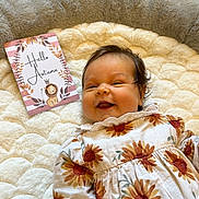 Esme is registered to the contest to win money with this photo: baby, infant, smiling, flower_pattern, outfit, blanket, soft_texture, card, autumn, lion_illustration, text, indoor, carpet, cute, child, happy, portrait, lying_down, cozy, warm_colors