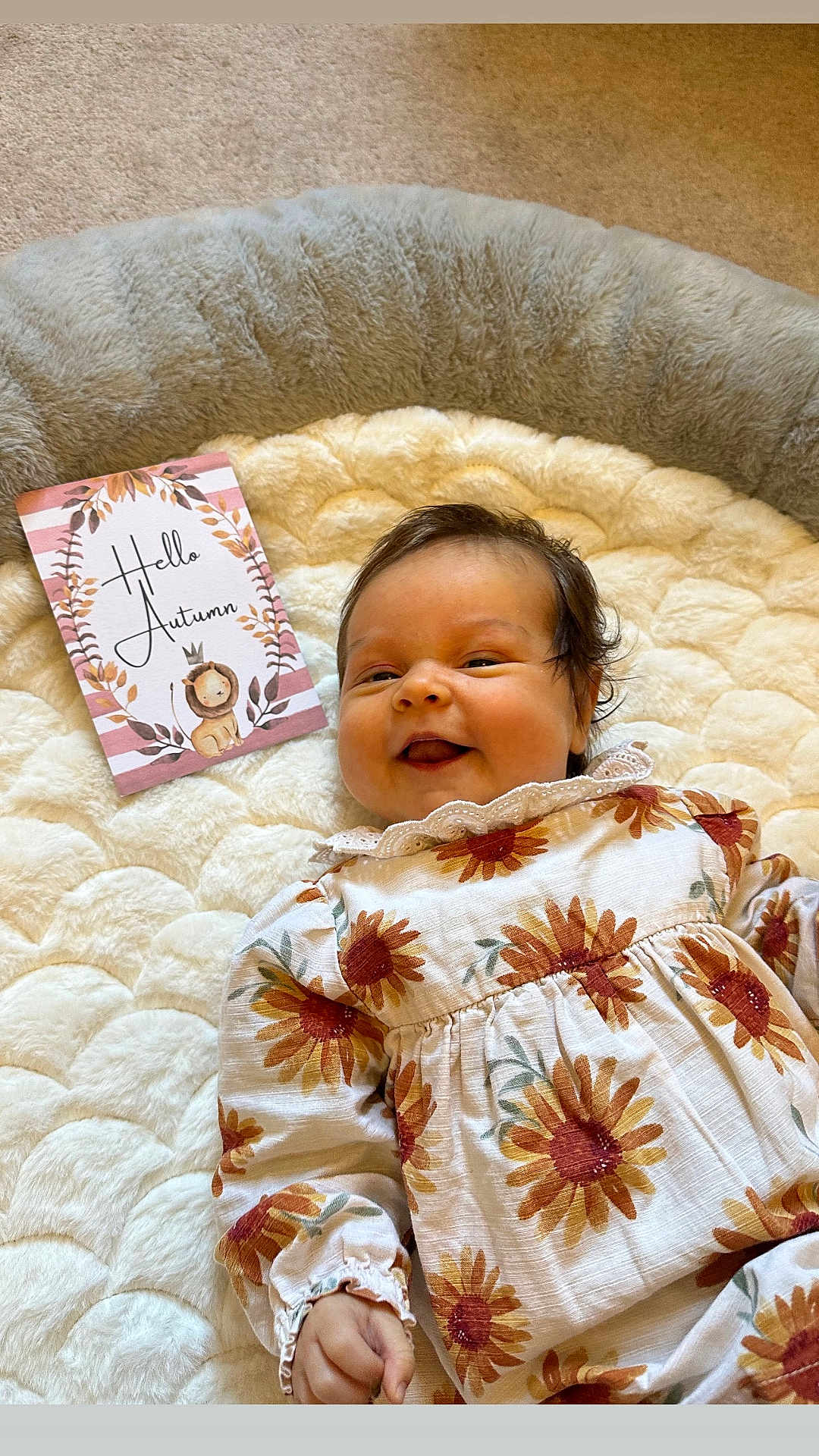 Esme is registered to the contest to win money with this photo: baby, infant, smiling, flower_pattern, outfit, blanket, soft_texture, card, autumn, lion_illustration, text, indoor, carpet, cute, child, happy, portrait, lying_down, cozy, warm_colors