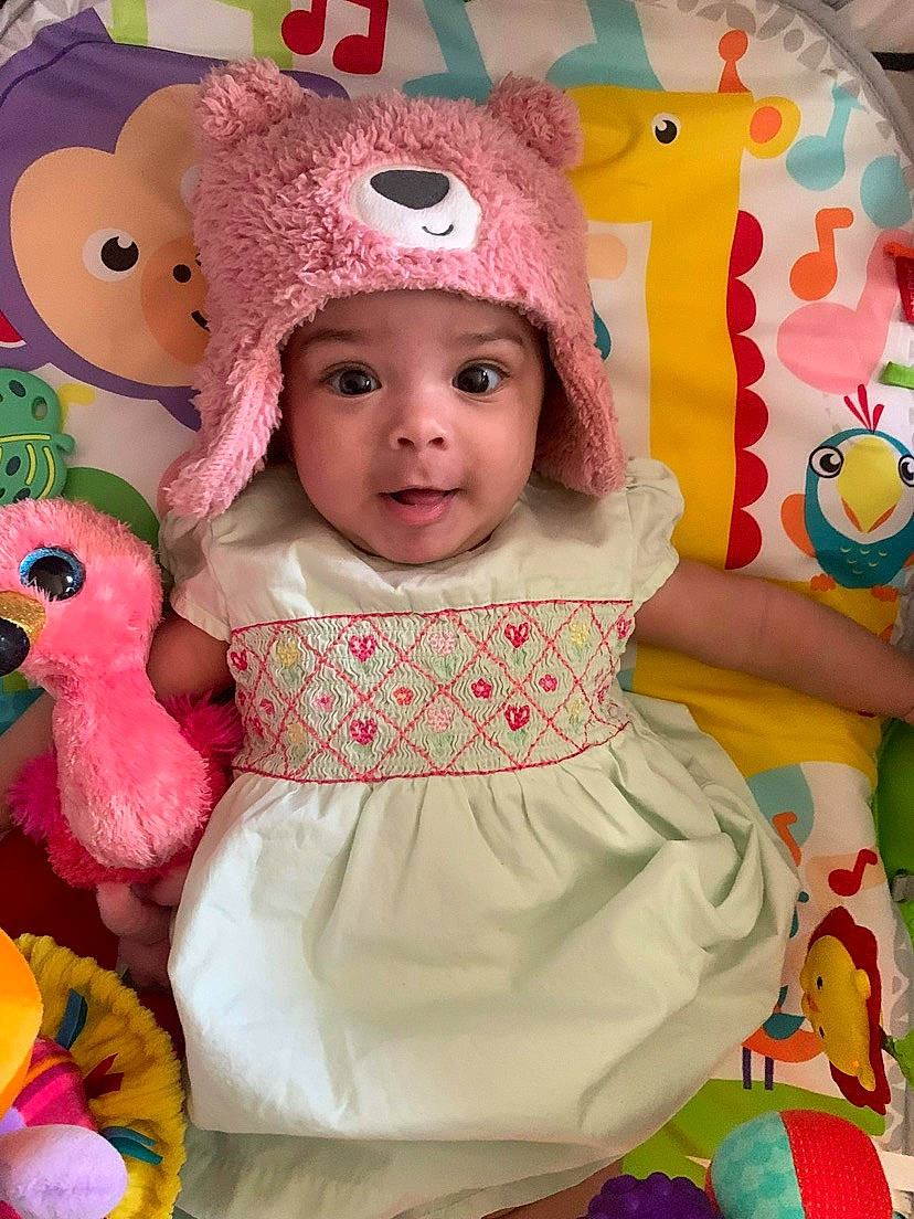 June is registered to the contest to win money with this photo: baby, baby_products, baby_toddler_clothing, beauty, cap, cheek, child, clothing, costume_hat, dress, happy, headwear, magenta, pattern, person, pink, skin, sleeve, textile, toddler