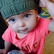 Oaklynn is registered to the contest to win money with this photo: child, toddler, blue_eyes, green_hat, pink_shirt, smile_text, curious, indoor, person, portrait, baby, cute, expression, face, hand, clothing, playful, floor, colorful_background, closeup