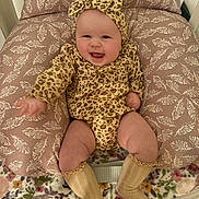 Catalina Ann is registered to the contest to win money with this photo: baby, smiling, leopard_print, headband, cushion, leaf_pattern, floral_blanket, socks, infant, cute, happy, indoors, child, clothing, seated, portrait, face, legs, cozy, warm