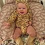 baby, child, clothing, cozy, cushion, cute, face, floral_blanket, happy, headband, indoors, infant, leaf_pattern, legs, leopard_print, portrait, seated, smiling, socks, warm