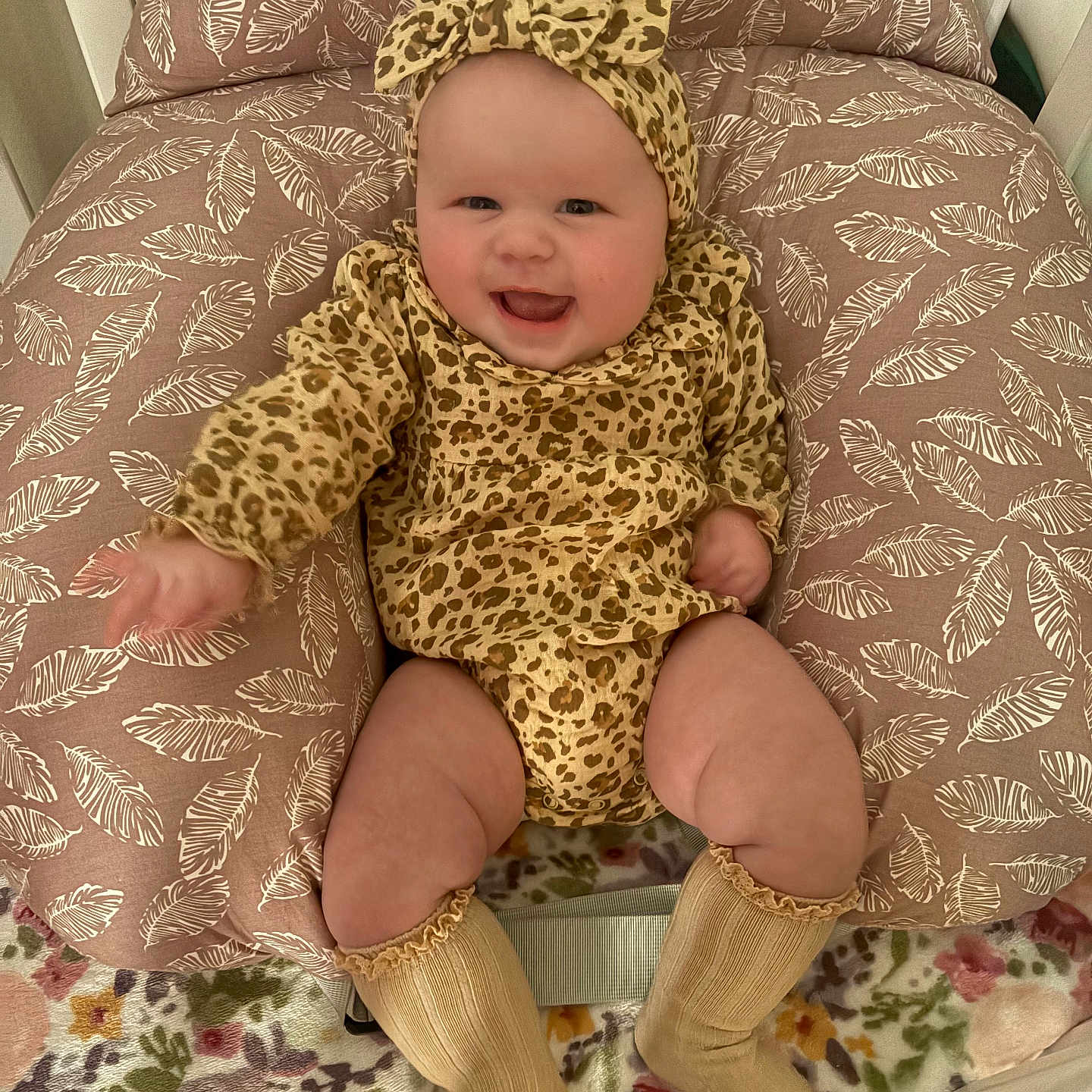 Catalina Ann is registered to the contest to win money with this photo: baby, child, clothing, cozy, cushion, cute, face, floral_blanket, happy, headband, indoors, infant, leaf_pattern, legs, leopard_print, portrait, seated, smiling, socks, warm
