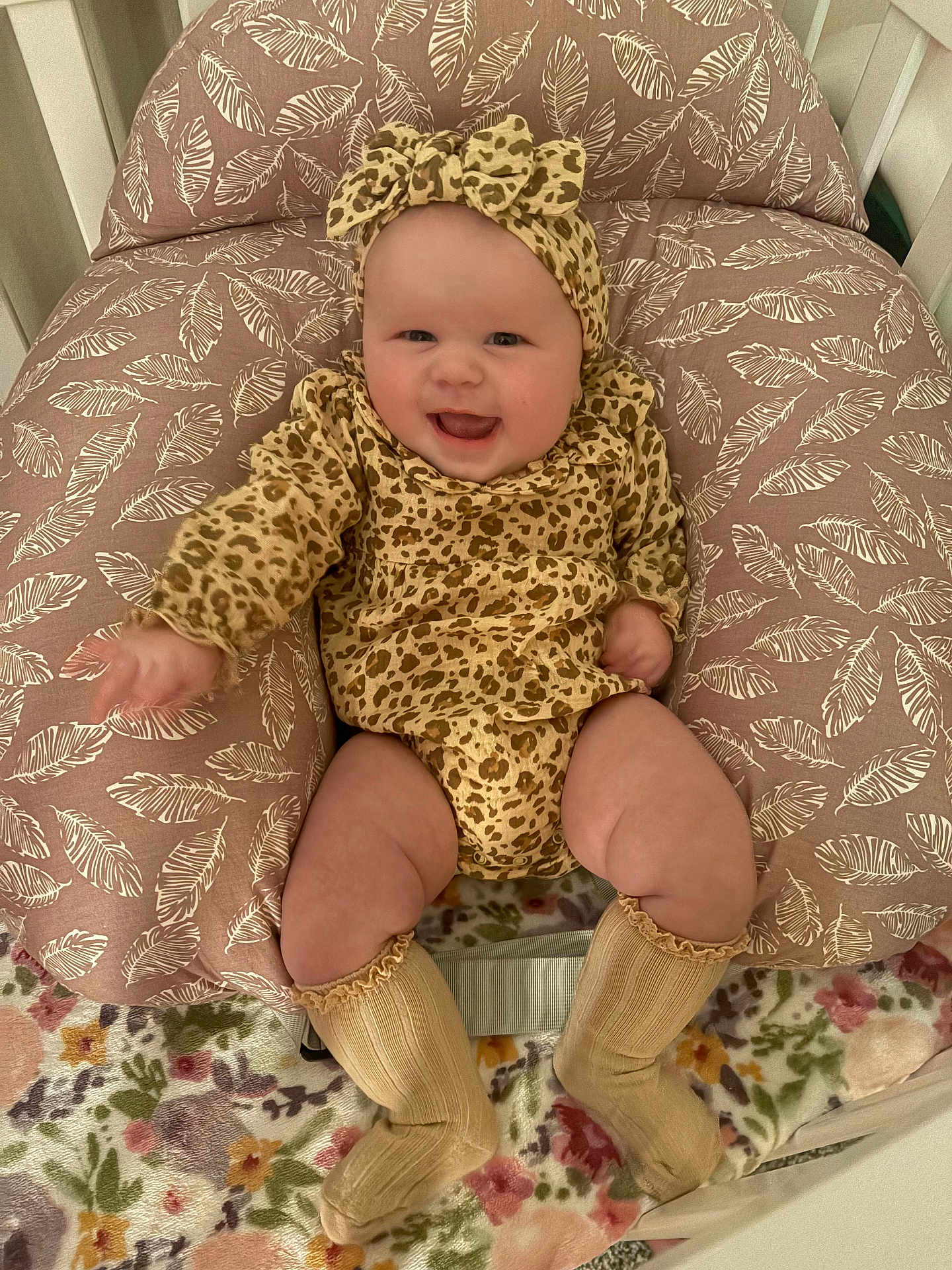Catalina Ann is registered to the contest to win money with this photo: baby, smiling, leopard_print, headband, cushion, leaf_pattern, floral_blanket, socks, infant, cute, happy, indoors, child, clothing, seated, portrait, face, legs, cozy, warm