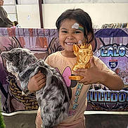Pinkerbell is registered to the contest to win money with this photo: animal, background, banner, cat, child, clothing, colorful, cute, event, face_paint, fluffy_cat, girl, happy, holding, indoor, pet, portrait, short_sleeve_shirt, smiling, trophy