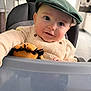 baby, child, cozy, cream_outfit, cute, face, furniture, green_cap, happy, headwear, high_chair, indoor, kitchen, person, plush_toy, portrait, seat, smiling, toy, young_child