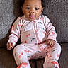 baby, child, pink_onesie, cherry_pattern, sitting, couch, gray_couch, curly_hair, adorable, indoor, portrait, infant, clothing, cute, person, smiling, face, young_child, comfort, home