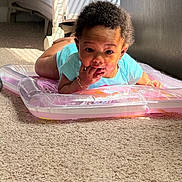 Adoree is registered to the contest to win money with this photo: baby, infant, child, carpet, indoor, inflatable, mat, blue_clothing, bracelet, hand, face, eyes, curly_hair, sunlight, floor, person, toddler, cute, lying_down, room