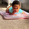 baby, infant, child, carpet, indoor, inflatable, mat, blue_clothing, bracelet, hand, face, eyes, curly_hair, sunlight, floor, person, toddler, cute, lying_down, room
