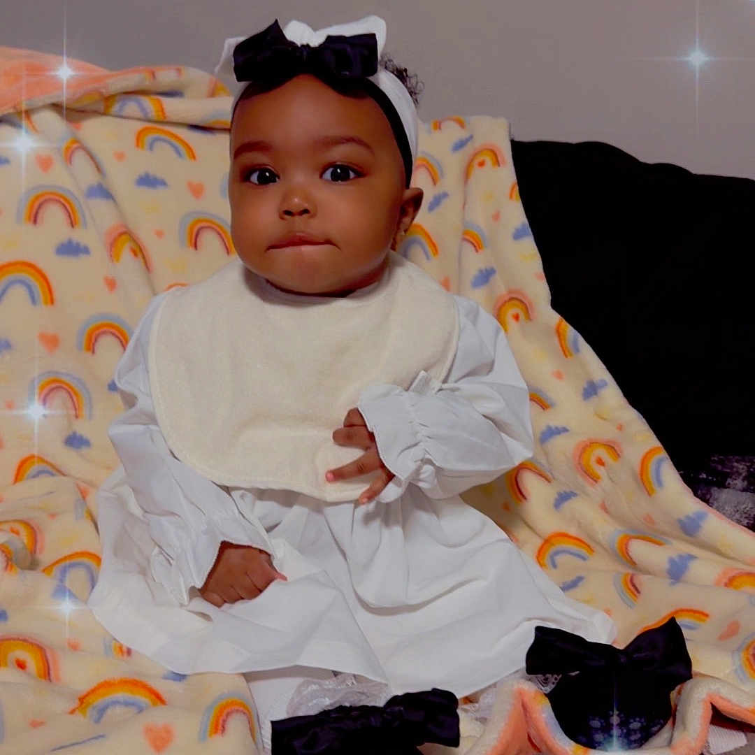 Zaior is registered to the contest to win money with this photo: adorable, baby, bib, black_bow, blanket, child, cozy, cute, face, headband, indoors, infant, portrait, rainbow_pattern, shoes, sitting, smiling, soft_texture, sparkle_effect, white_dress