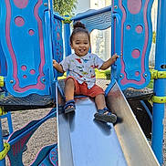 Kayron participe au concours pour gagner de l'argent avec cette photo : child, toddler, smiling, playground, slide, outdoor, summer, happy, person, clothing, shorts, shirt, sand, feet, sandals, metal, fun, play, sunlight, nature