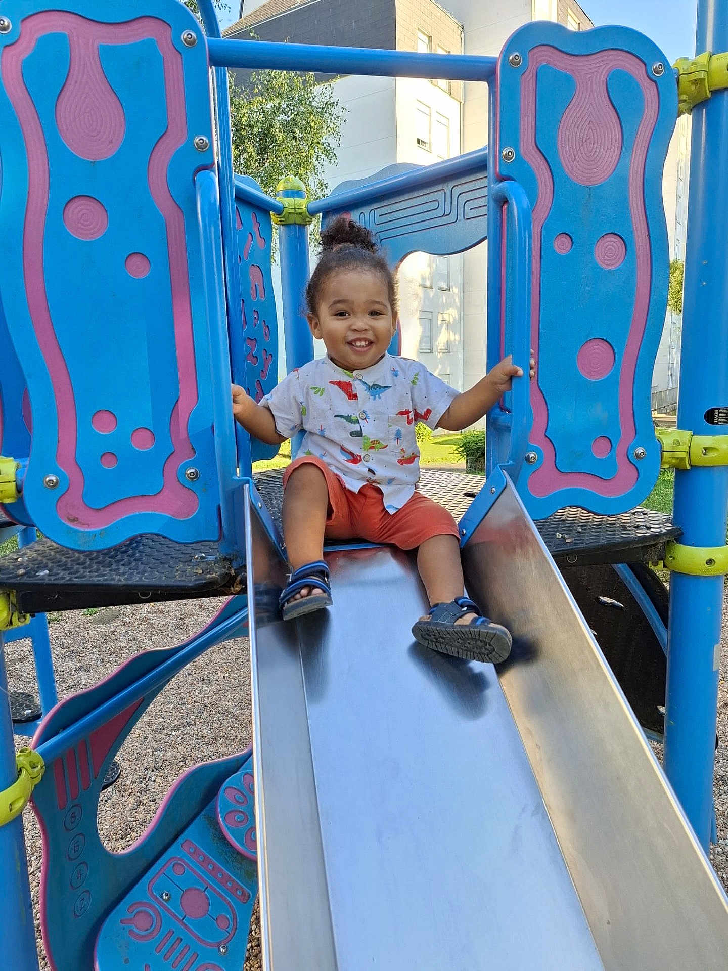 Kayron participe au concours pour gagner de l'argent avec cette photo : child, toddler, smiling, playground, slide, outdoor, summer, happy, person, clothing, shorts, shirt, sand, feet, sandals, metal, fun, play, sunlight, nature