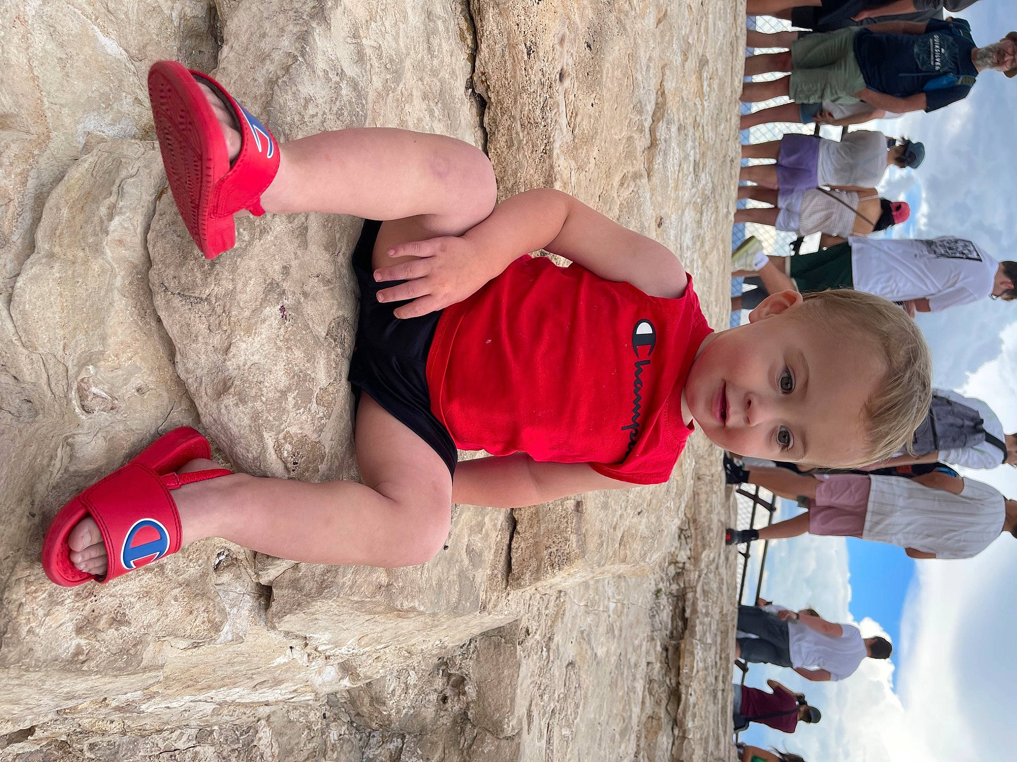 Hayden is registered to the contest to win money with this photo: beach, beauty, blue, eyewear, foot, fun, hand, hat, headwear, human_leg, knee, leg, leisure, person, sand, shorts, t_shirt, thigh, toddler, trunk