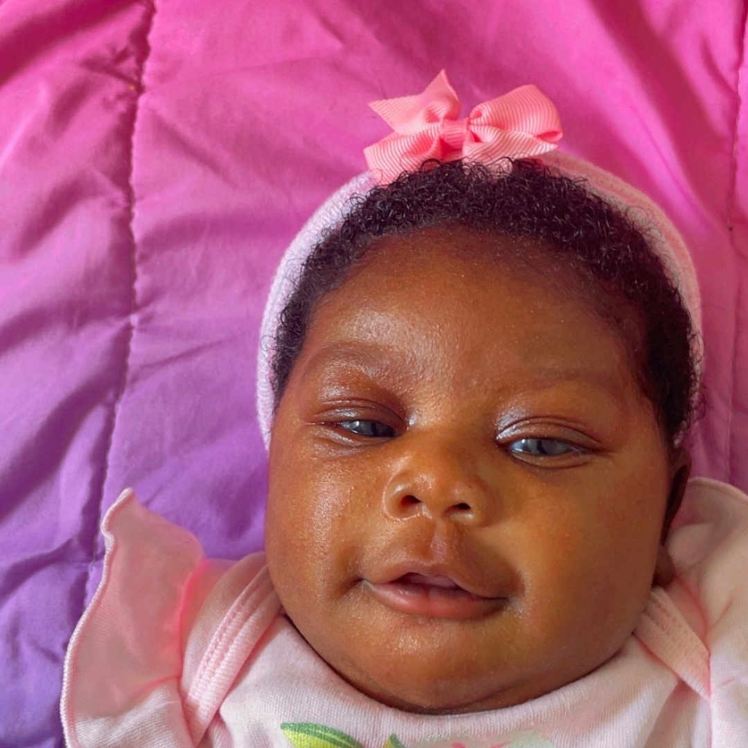 Amara joined the competition — help win amazing prizes! baby, blanket, bow, child, closeup, cute, floral_clothing, hand, headband, indoors, infant, newborn, person, pink, portrait, resting, skin, sleepwear, smile, soft