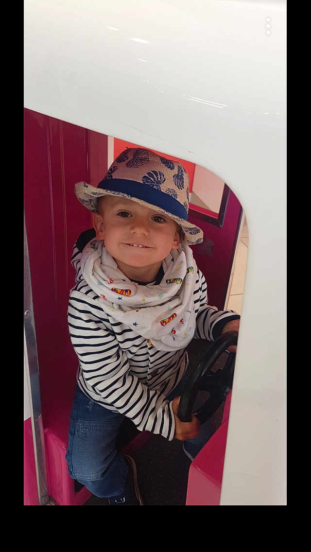 Julian participe au concours pour gagner de l'argent avec cette photo : child, hat, striped_clothing, scarf, steering_wheel, play_structure, indoor, smiling, jeans, sitting, person, casual_wear, cute, young, fun, playful, happy, portrait, hat_pattern, colorful