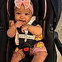baby, child, car_seat, pink_bow, bracelet, smile, happy, infant, clothing, sitting, cute, indoors, safety_harness, portrait, person, toddler, playful, cartoon_print, headband, closeup