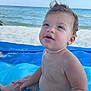 toddler, child, beach, ocean, sand, water, blue_blanket, curly_hair, bare_chest, summer, outdoor, sea, waves, sunny, young_child, playful, vacation, nature, happy, relaxed