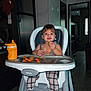 toddler, child, high_chair, snack, kitchen, food, sippy_cup, legs, feet, plaid_pants, indoor, person, face, happy, eating, tray, baby, footrest, hair, room