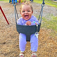 Millie is registered to the contest to win money with this photo: toddler, child, swing, playground, purple_clothing, unicorn_pattern, smiling, happy, outdoor, play, sand, grass, footwear, sandals, chain, park, daylight, person, toy, fun